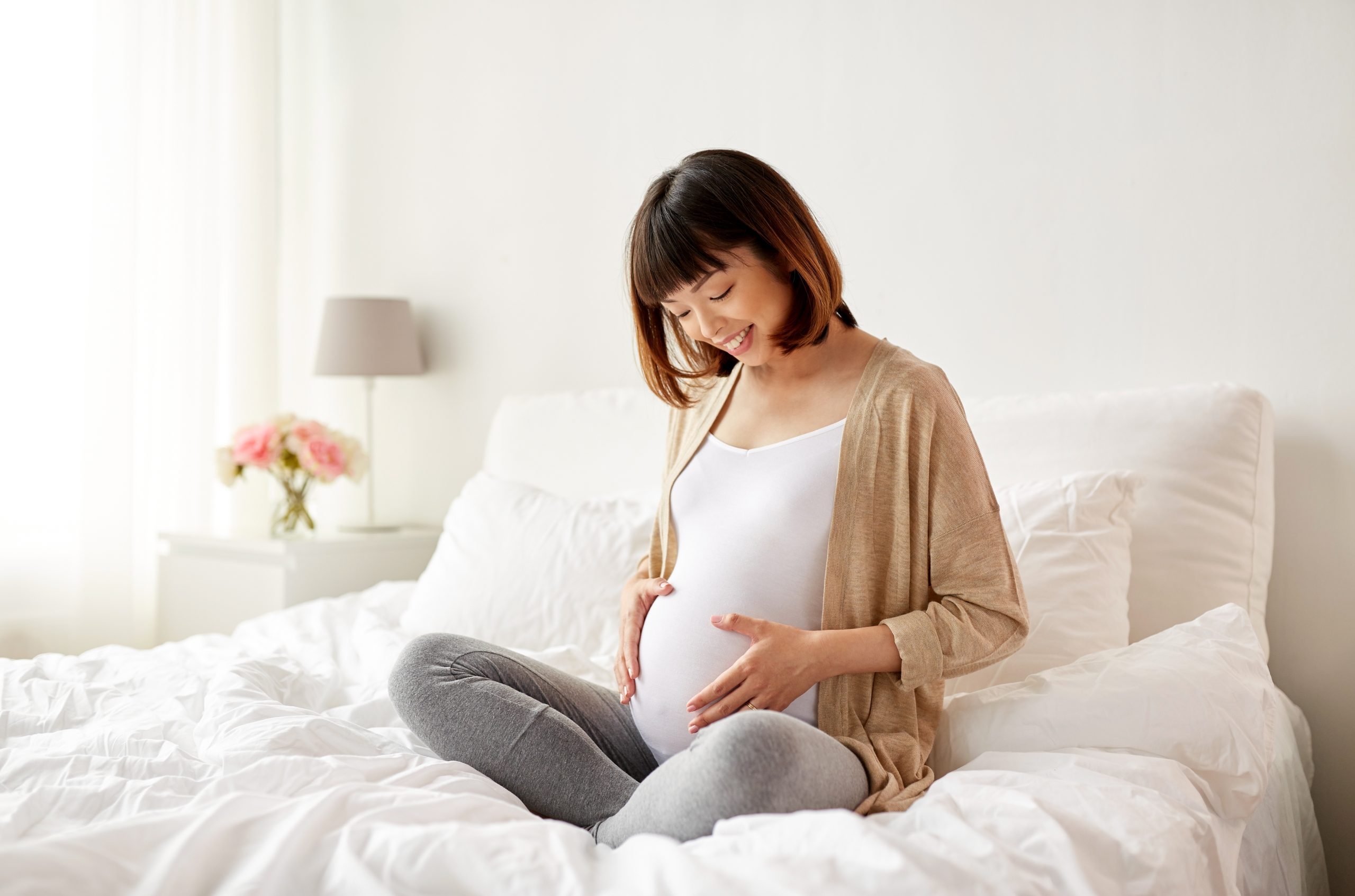 happy pregnant asian woman sitting in bed at home